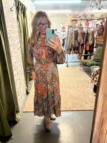 Woman wearing The Midnight Meadow Dress—maxi length, patchwork floral print, tie neck, elastic waist, styled with boots.