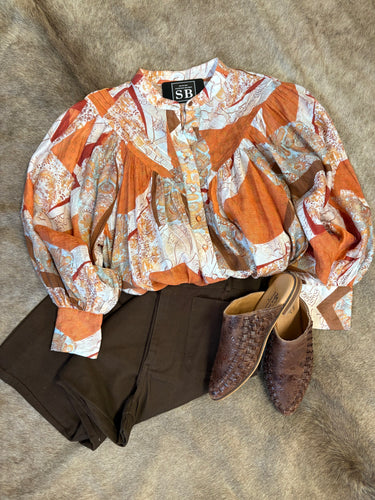 Lightweight rust and ivory blouse with button detail, generous fit and voluminous sleeves, styled with dark pants and mules.