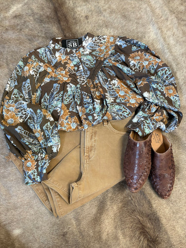Dark brown floral blouse with white, blue, and tan blooms, oversized fit and button detail, styled with crop jeans.