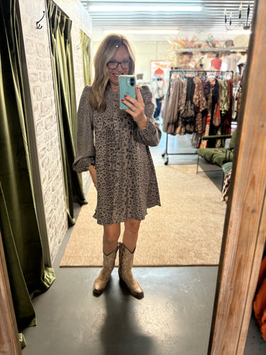 Woman wearing The Laredo Leopard Dress—leopard print, button front, roomy fit with pockets, styled with cowgirl boots.