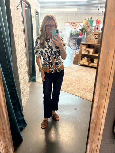 Blue floral fitted blouse with cinched waist and contrast hem, styled with jeans and sandals.
