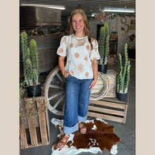 Load image into Gallery viewer, Woman wearing a cream blouse with rust floral embroidery and puff sleeves, standing by cacti and a wooden wagon wheel on a cowhide rug.
