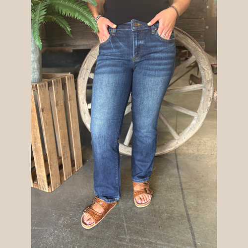 Woman wearing dark wash ankle-length jeans with clean hem, standing in front of a rustic wagon wheel.