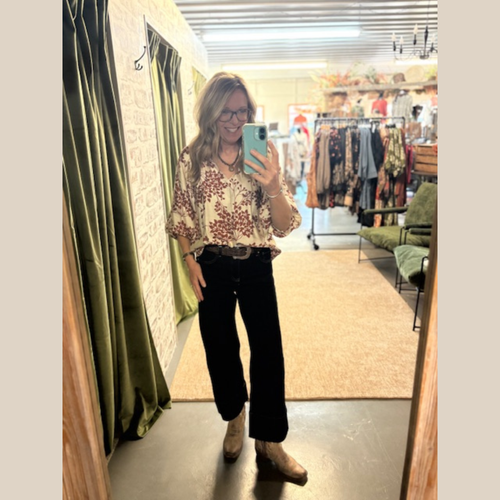 Woman wearing cream blouse with burgundy floral print, wide sleeves, and v-neckline.