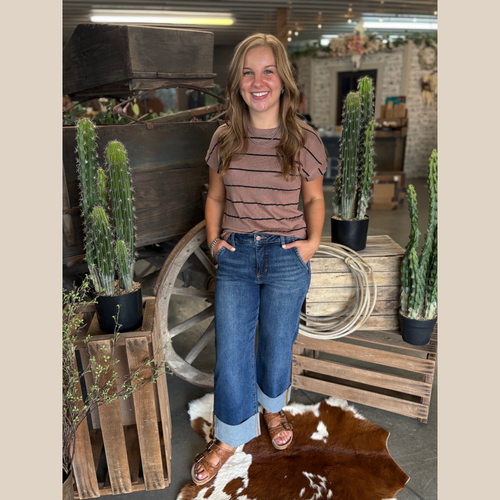 Woman wearing the Striped Espresso Top with cropped denim and sandals, standing in front of a rustic wooden wagon.