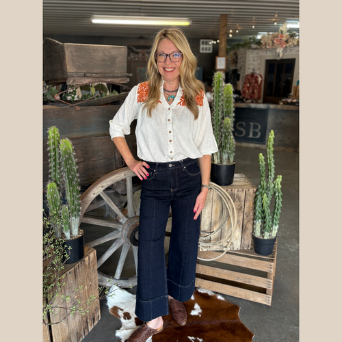 White split-neck top with wooden buttons, rust floral embroidery on shoulders, and three-quarter sleeves.