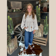 Load image into Gallery viewer, Oat and mocha striped babydoll top with tassel ties, balloon sleeves, and wide-leg jeans in a western boutique setting.
