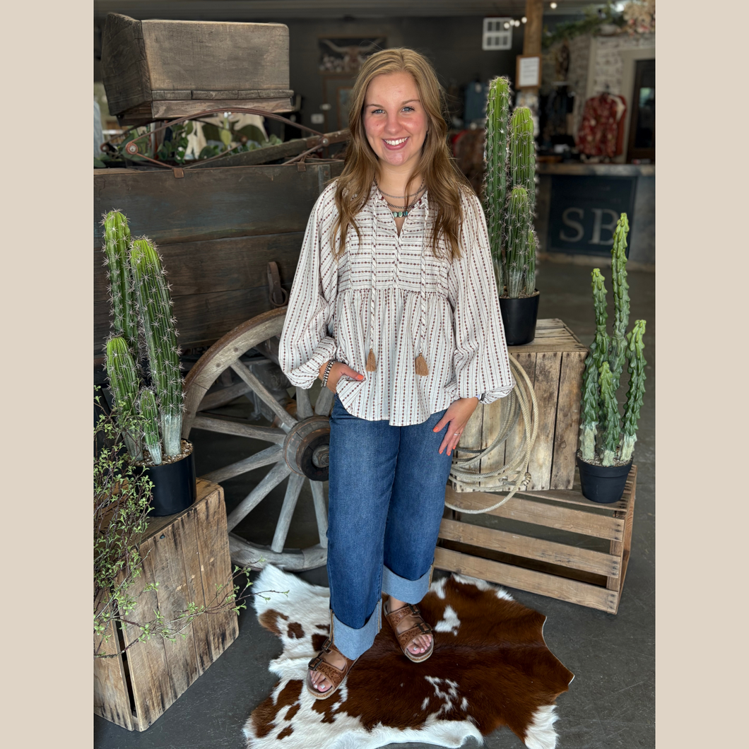 Oat and mocha striped babydoll top with tassel ties, balloon sleeves, and wide-leg jeans in a western boutique setting.