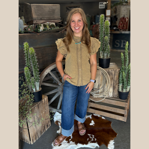 Golden-brown button-up top with ruffle sleeves, worn with wide-leg jeans and turquoise jewelry in a western boutique.
