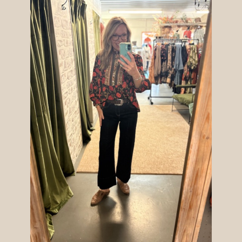 Woman wearing black floral blouse with patterned trim, relaxed fit, and long sleeves.