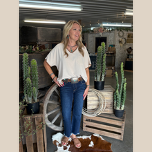 Load image into Gallery viewer, Woman wearing a V-neck blouse with contrasting whipstitch detail, shown in oatmeal and mocha colors, styled in a western indoor setting.
