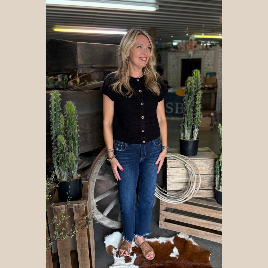 Woman wearing The Willow Knit Vest with cropped jeans, standing in front of a rustic wooden wagon.